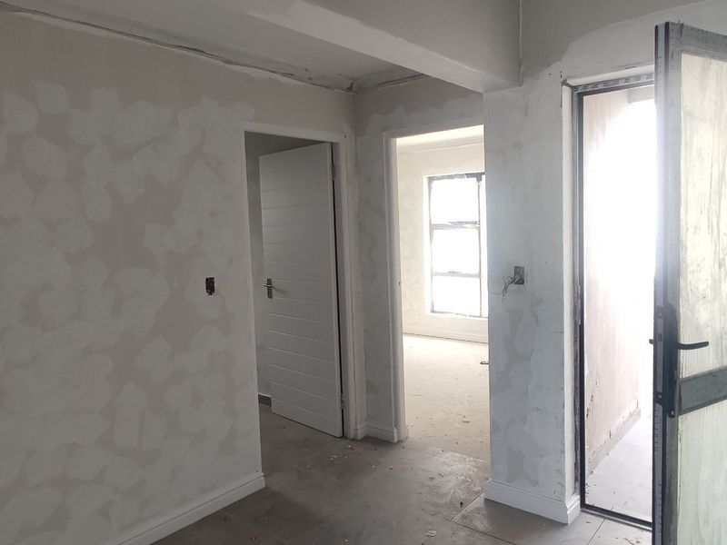A hallway area currently under renovation with unfinished plasterwork on the walls and exposed electrical points, awaiting final finishes.