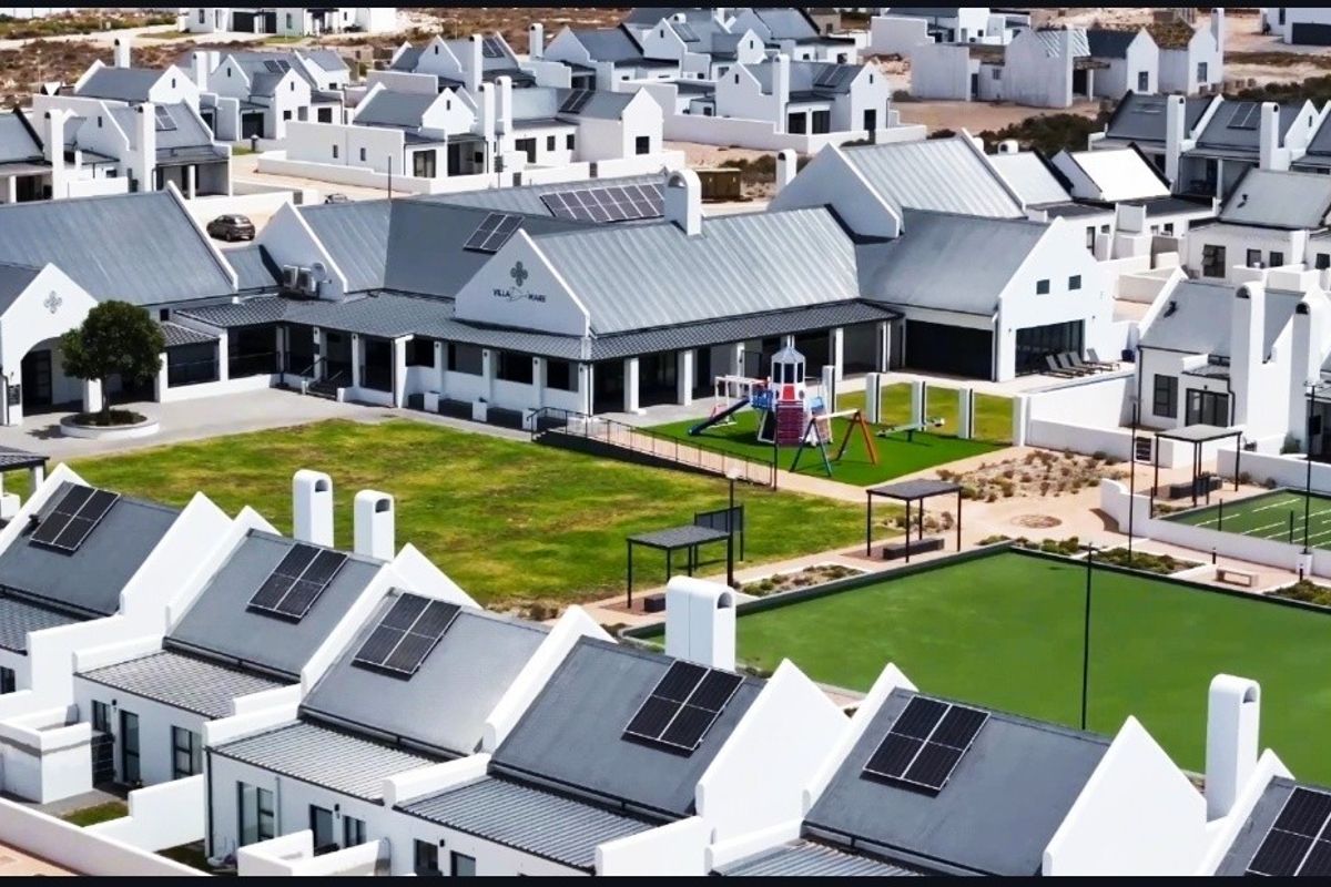 Aerial view of a residential estate featuring modern white houses with metal roofs, solar panels, communal green spaces, and recreational facilities.