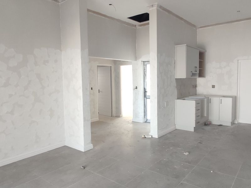 An open-plan living and kitchen area currently under construction, featuring tiled floors, unfinished wall surfaces, and partially installed kitchen cabinetry.