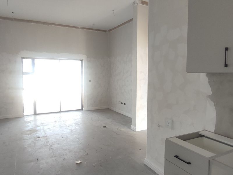 An unfinished open-plan living and kitchen area featuring tiled floors, built-in cabinetry, and a large sliding glass door leading to the exterior.
