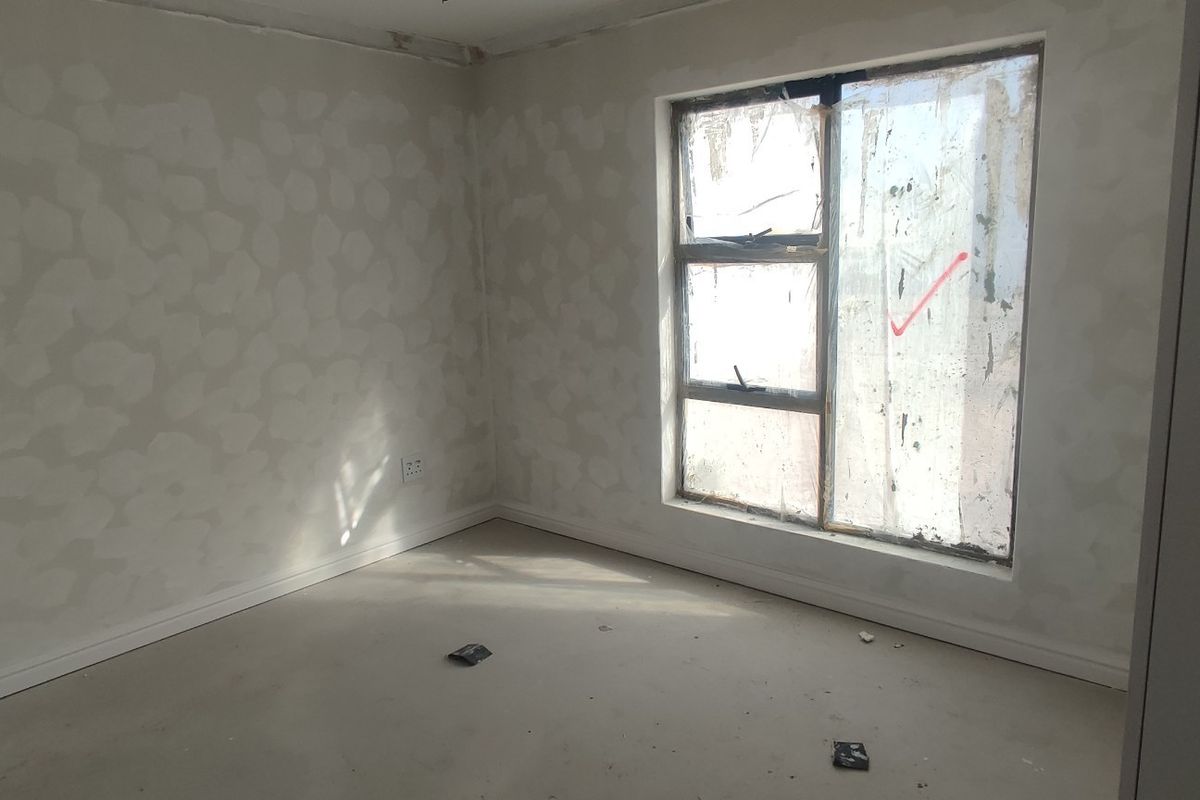 An unfinished bedroom interior featuring bare plastered walls, skirting boards, and an aluminium window frame, currently in a state of renovation.