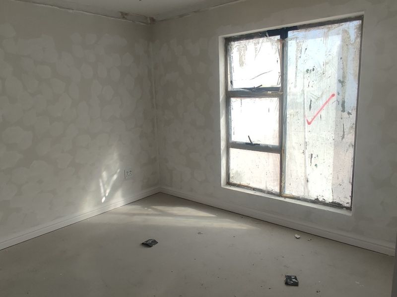 An unfinished bedroom interior featuring bare plastered walls, skirting boards, and an aluminium window frame, currently in a state of renovation.