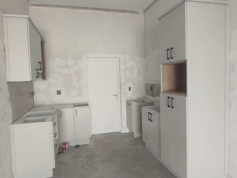 An unfinished kitchen space featuring installed cabinetry and tiled flooring, currently awaiting final wall finishes and appliance installation.