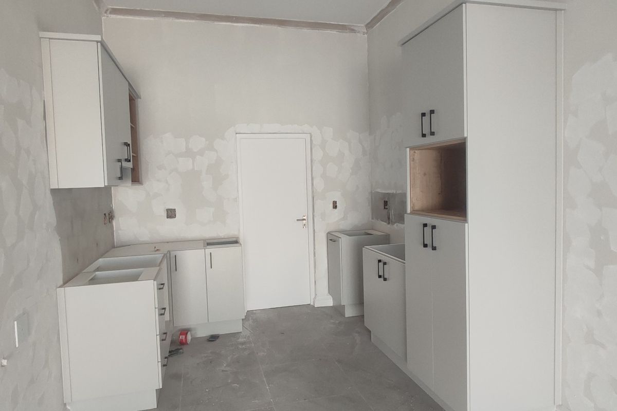 An unfinished kitchen space featuring installed cabinetry and tiled flooring, currently awaiting final wall finishes and appliance installation.