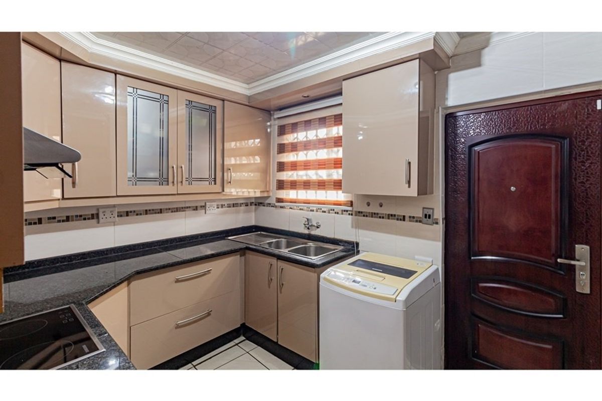 A compact, well-maintained kitchen featuring modern high-gloss cabinetry, granite countertops, a double basin sink, and integrated extractor fan.