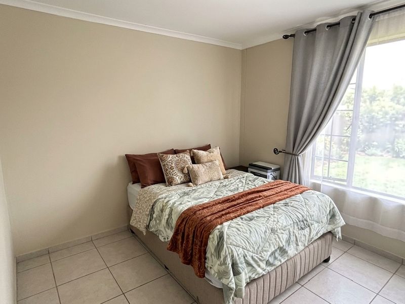 A bedroom featuring neutral wall tones, tiled flooring, and a large window that allows for natural light.