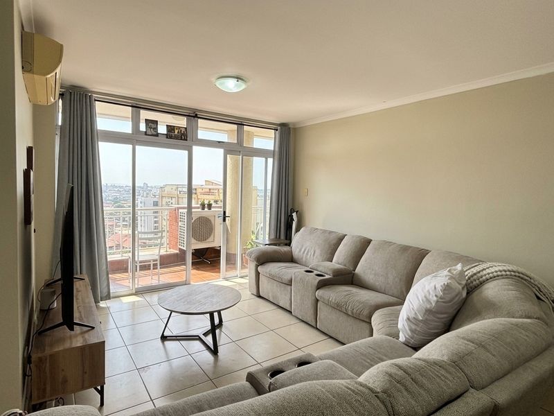 A bright living room featuring tiled flooring and large sliding glass doors that provide access to a balcony with city views.