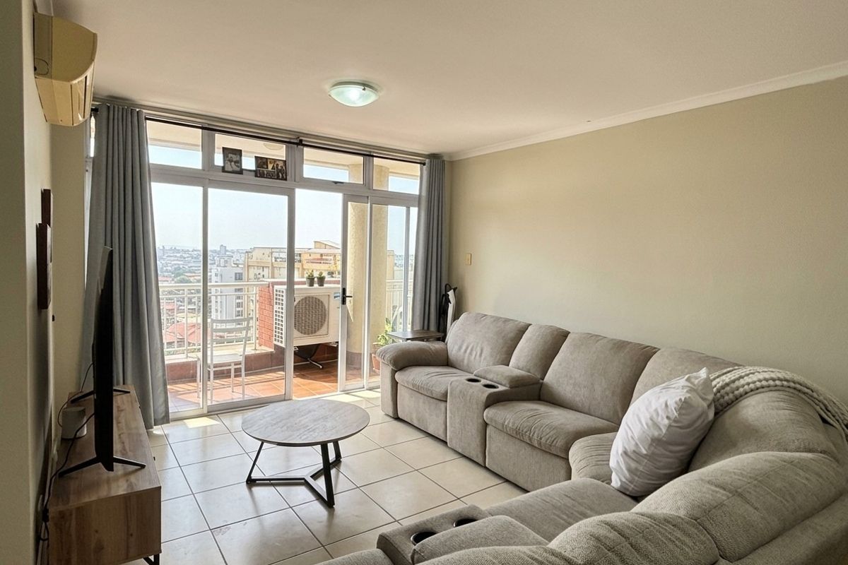 A bright living room featuring tiled flooring and large sliding glass doors that provide access to a balcony with city views.