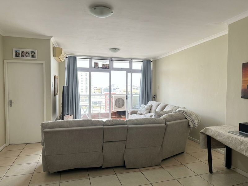 A bright living room featuring tiled flooring, a wall-mounted air conditioning unit, and large sliding glass doors leading to a balcony.