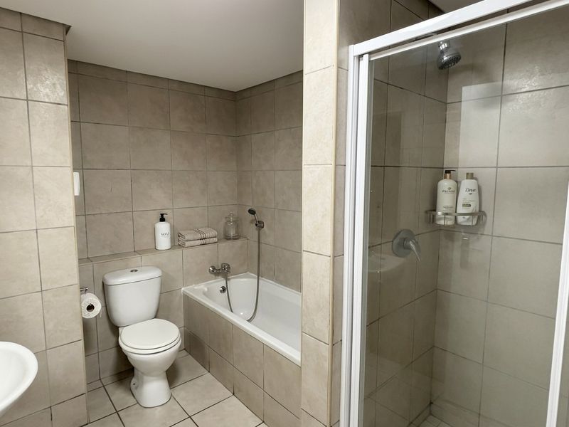 A functional bathroom featuring a built-in bathtub, separate shower enclosure, and neutral ceramic tiling throughout.