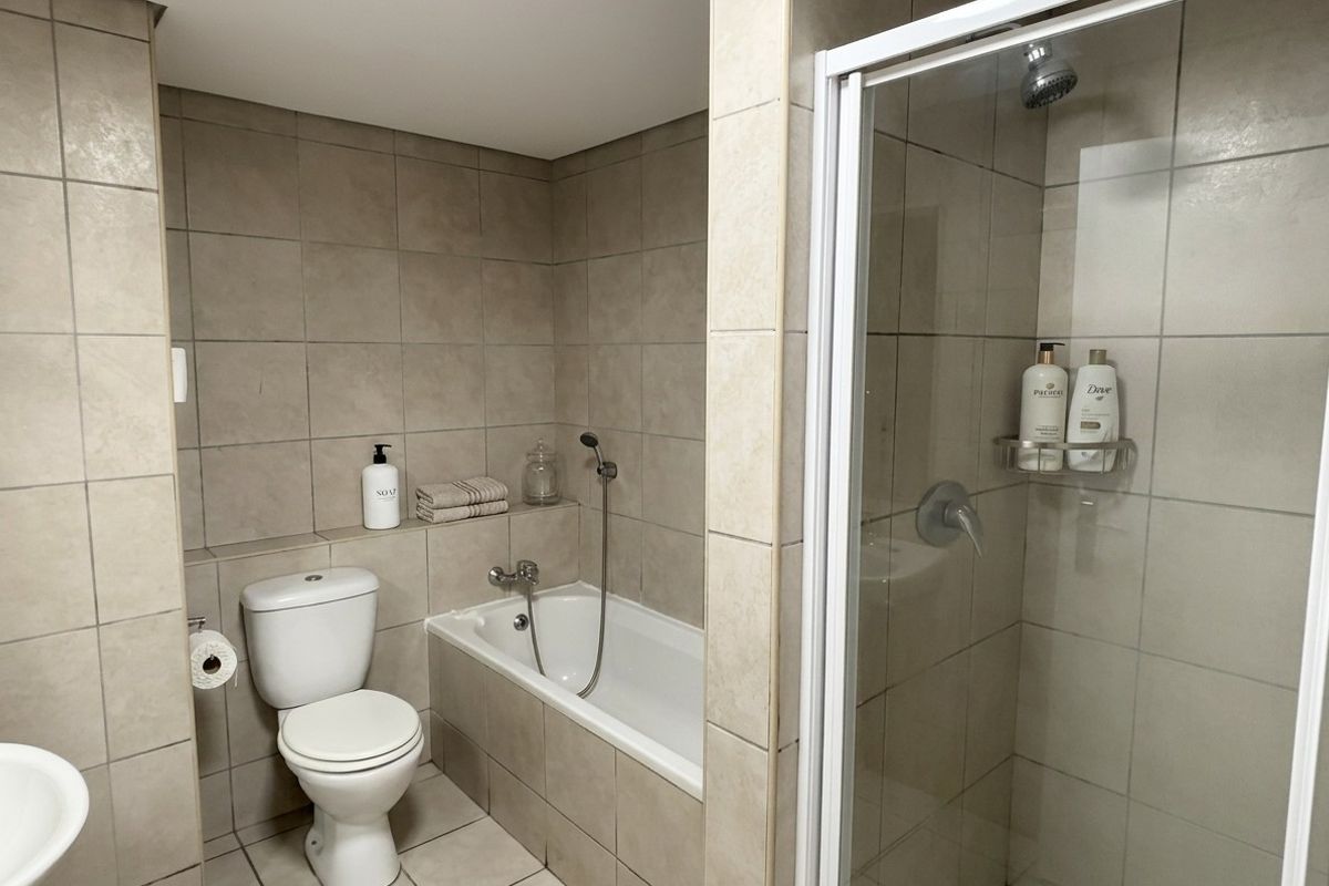 A functional bathroom featuring a built-in bathtub, separate shower enclosure, and neutral ceramic tiling throughout.
