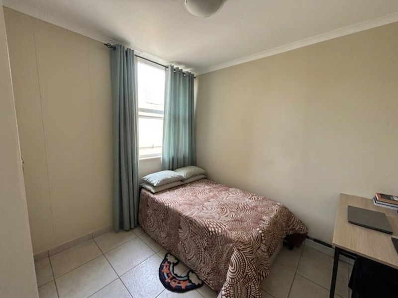 A compact bedroom featuring tiled flooring, neutral wall finishes, and a window with curtains, providing a functional living space.