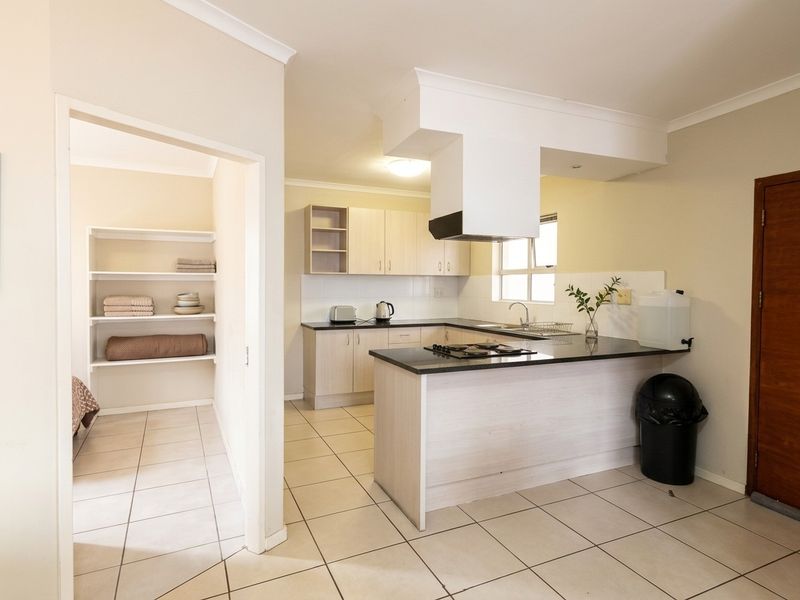 Functional kitchen featuring light wood cabinetry, dark laminate countertops, gas hob, extractor fan, and an adjacent walk-in pantry or storage area with built-in shelving.