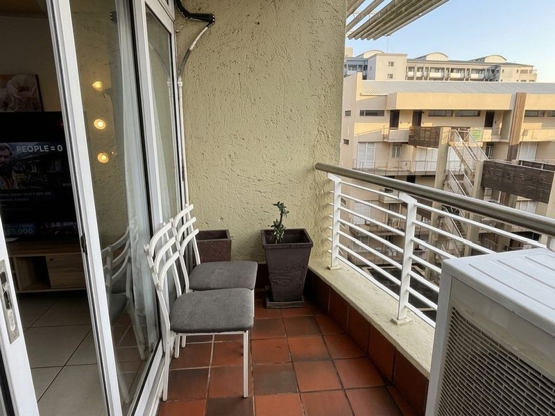 A compact balcony featuring terracotta tiling, a metal safety balustrade, and an integrated air conditioning unit, offering an outdoor extension to the living area.