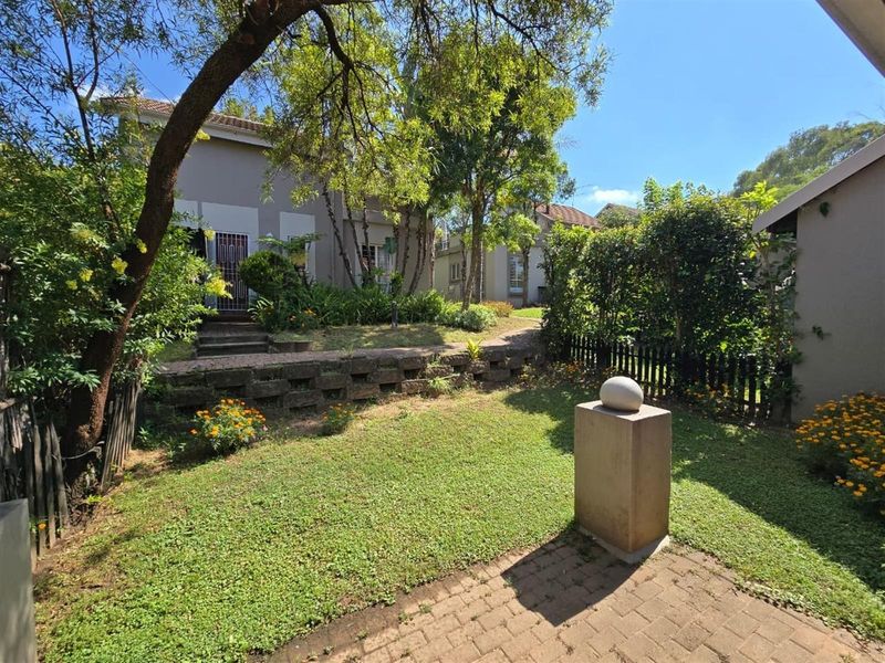 A well-maintained private garden featuring a paved patio area, tiered landscaping with a retaining wall, and established trees and shrubs.