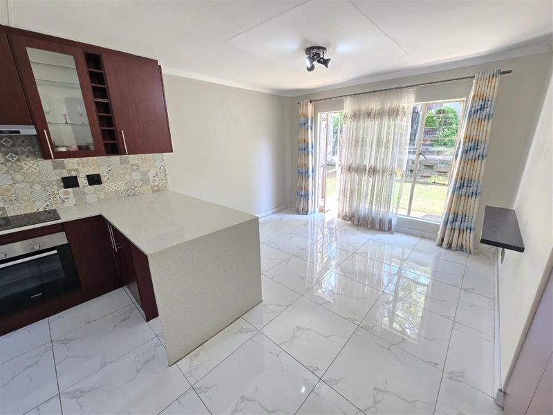 Open-plan kitchen and living area featuring modern tiled flooring, stone countertops, built-in cabinetry, and direct access to the garden through a glass sliding door.