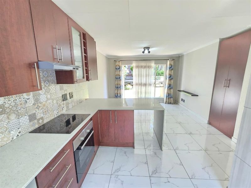 Open-plan kitchen and living area featuring modern cabinetry, stone countertops, built-in appliances, and large format marble-look floor tiles leading to a patio.