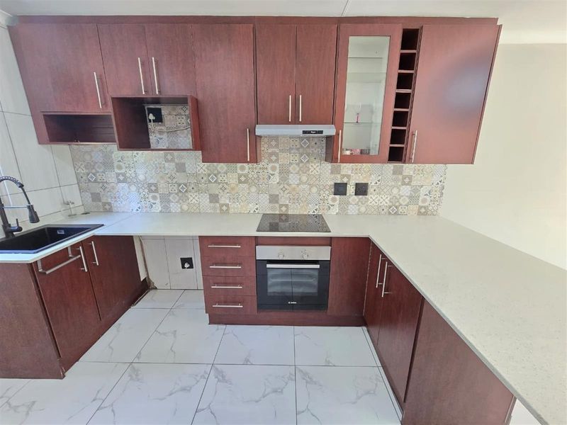 A modern kitchen featuring dark wood cabinetry, stone countertops, a patterned tile backsplash, and integrated appliances including an oven and electric hob.