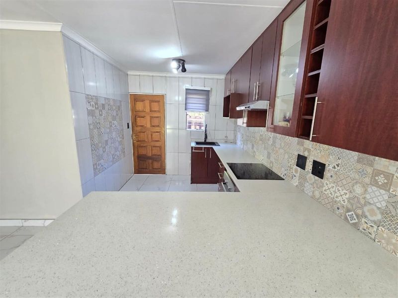 A modern kitchen featuring dark wood cabinetry, light stone countertops, a built-in electric hob with extractor, and decorative tiled backsplash.