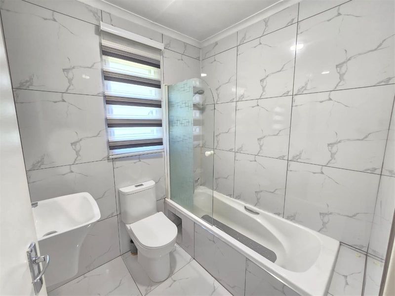 Modern bathroom featuring floor-to-ceiling marble-look tiling, a pedestal basin, toilet, and a bathtub with a glass shower screen.