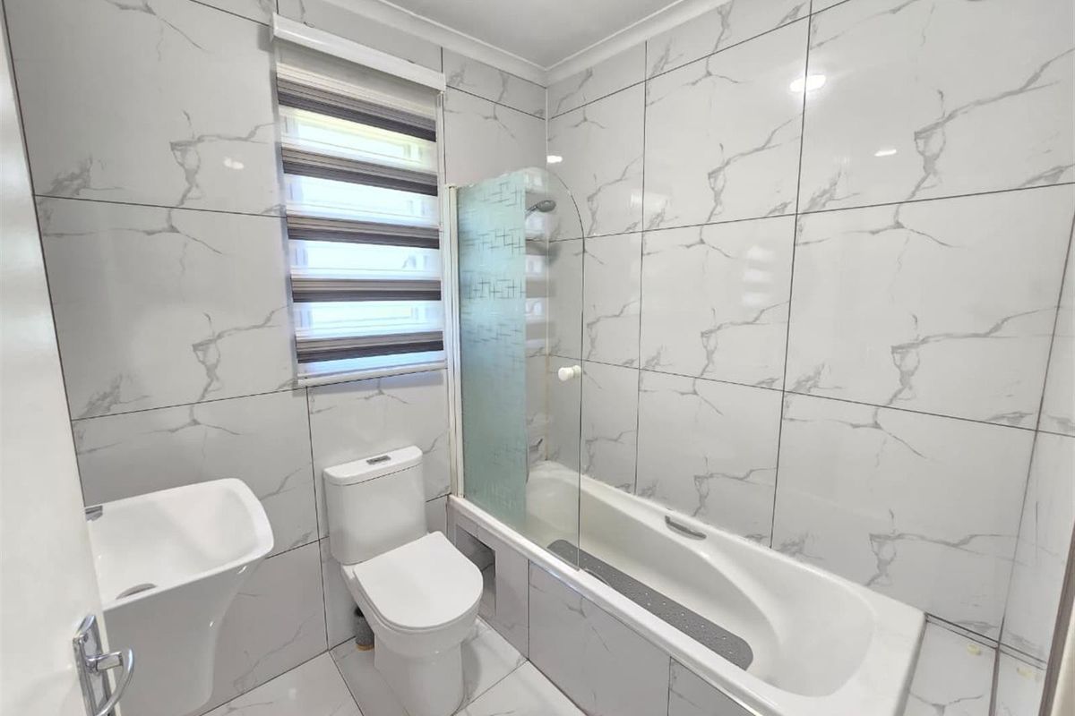 Modern bathroom featuring floor-to-ceiling marble-look tiling, a pedestal basin, toilet, and a bathtub with a glass shower screen.