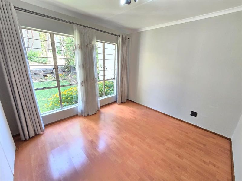 A bright, empty bedroom featuring laminate flooring, large windows with security bars, and neutral wall finishes, offering a clean canvas for personalization.