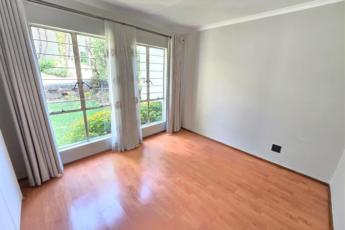 A bright, empty bedroom featuring laminate flooring, large windows with security bars, and neutral wall finishes, offering a clean canvas for personalization.
