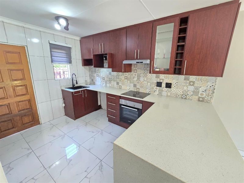 Modern kitchen featuring dark wood cabinetry, stone countertops, integrated electric hob and oven, tiled backsplash, and polished floor tiles.