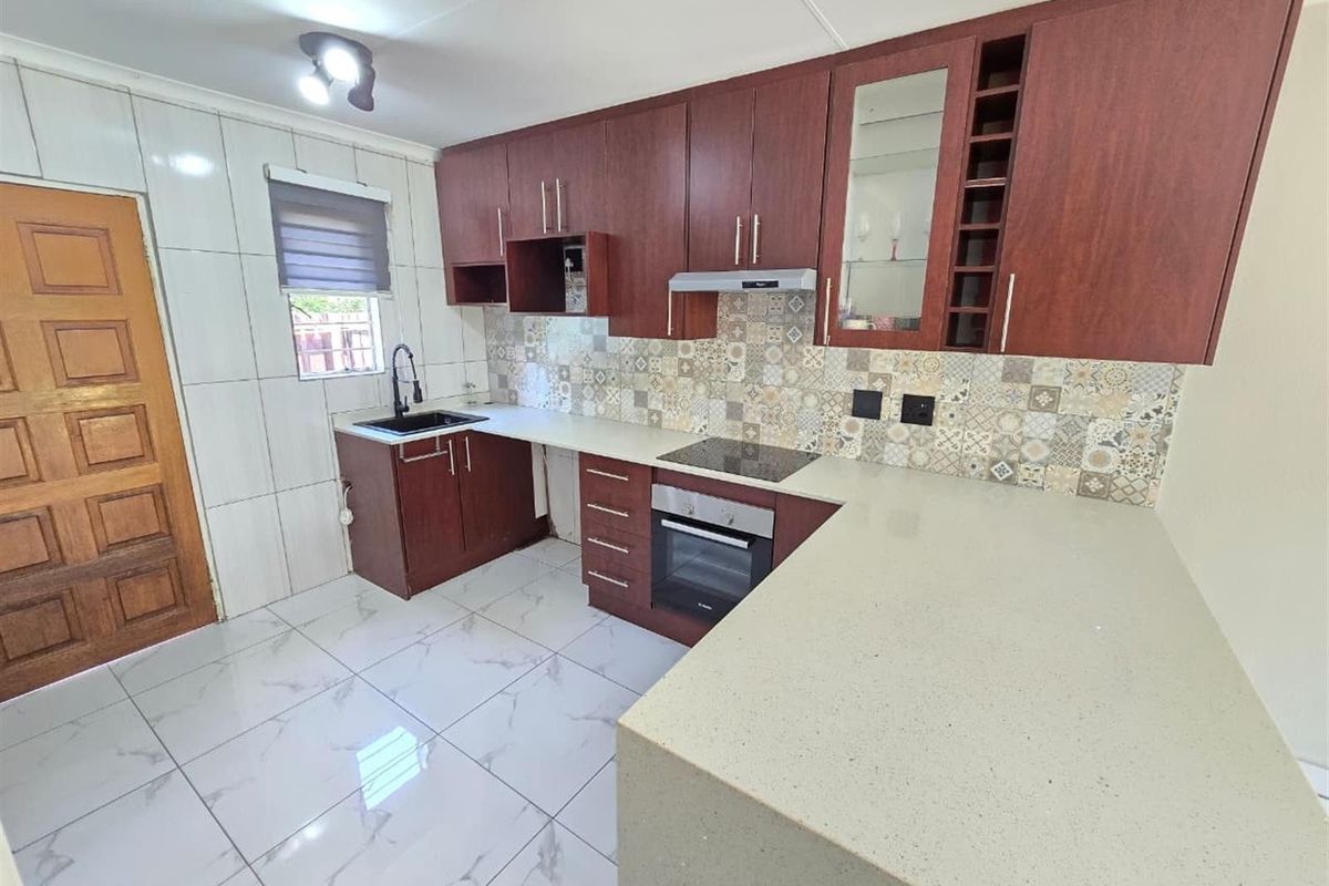 Modern kitchen featuring dark wood cabinetry, stone countertops, integrated electric hob and oven, tiled backsplash, and polished floor tiles.