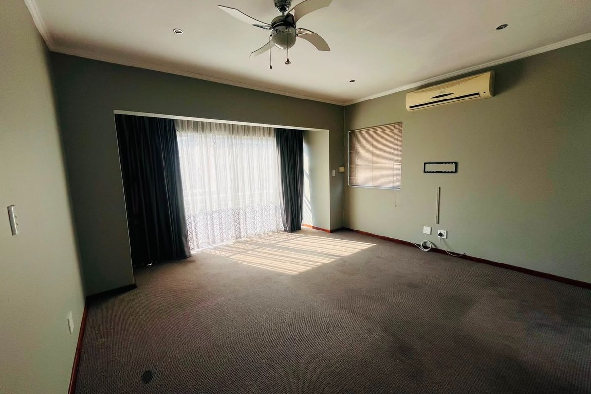 Spacious living room featuring neutral walls, carpet flooring, a ceiling fan, and a wall-mounted air conditioning unit with large sliding door access.