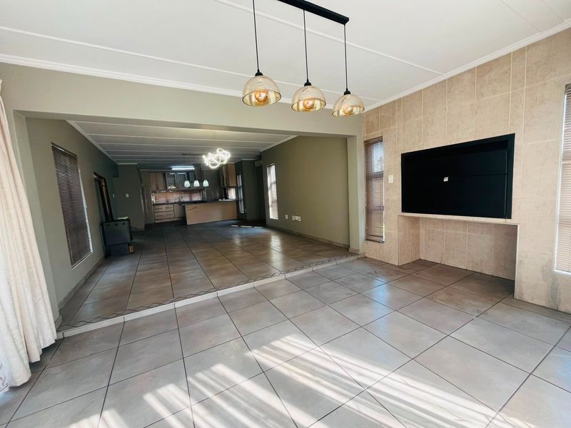 Spacious open-plan living and kitchen area featuring large format floor tiles, a built-in fireplace, and modern pendant lighting.