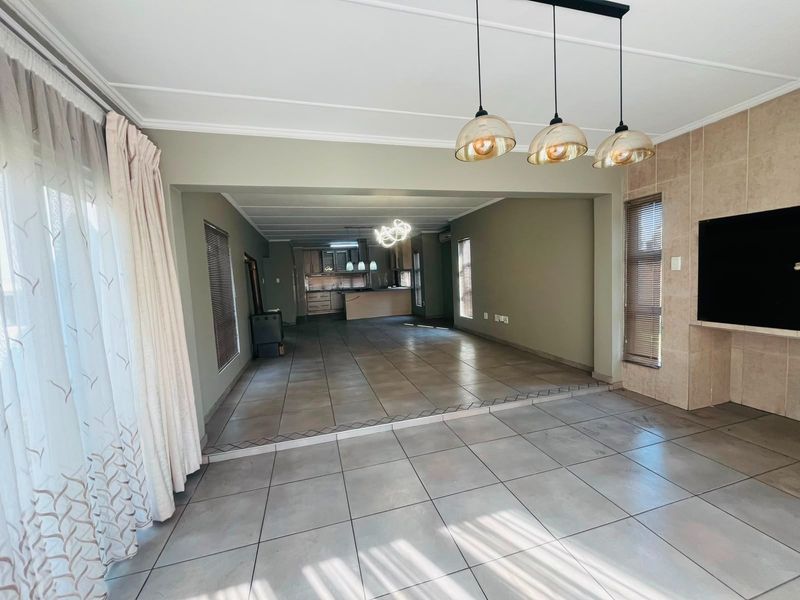Spacious open-plan living and kitchen area featuring large format floor tiles, a built-in fireplace with tiled surround, and modern pendant lighting.