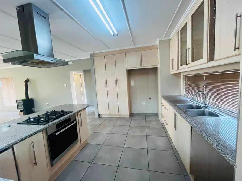 Spacious kitchen featuring granite countertops, built-in oven, gas hob, stainless steel extractor fan, and ample cabinetry, with tiled flooring and an adjacent wood burning stove.
