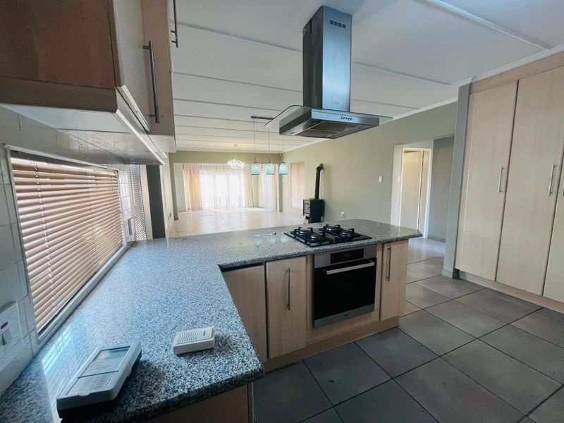 Spacious open-plan kitchen and living area featuring granite countertops, a gas hob, built-in oven, and a cozy wood-burning fireplace.