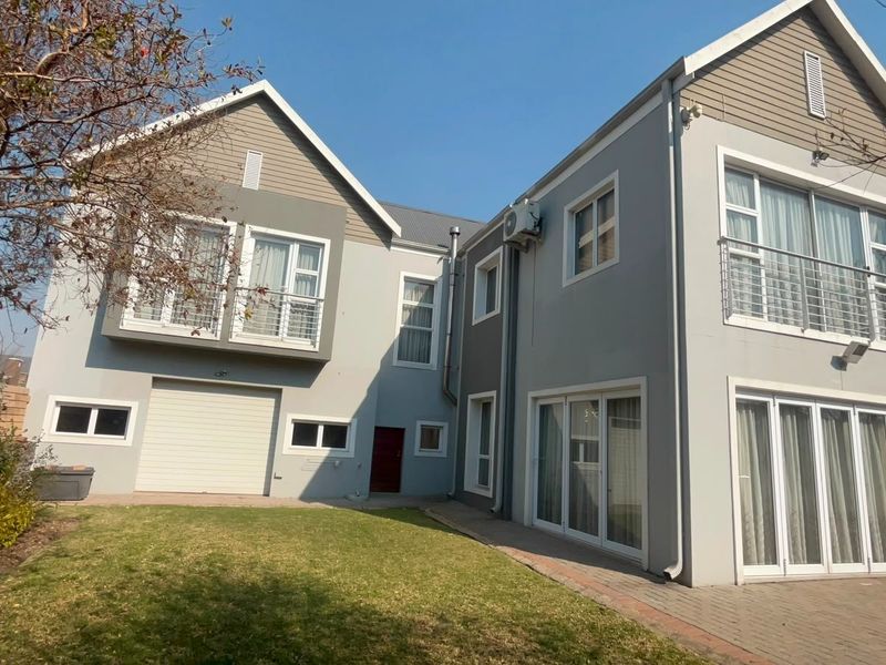 Rear view of a two-story residential property featuring a paved patio, lawn area, balcony, and integrated garage.