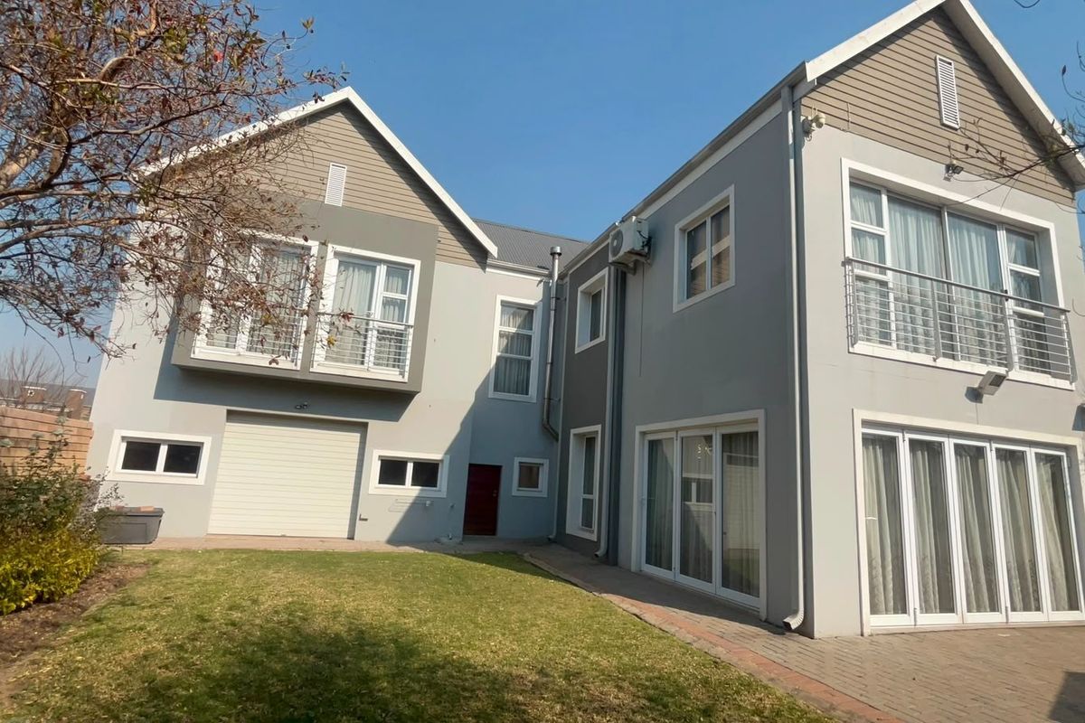 Rear view of a two-story residential property featuring a paved patio, lawn area, balcony, and integrated garage.