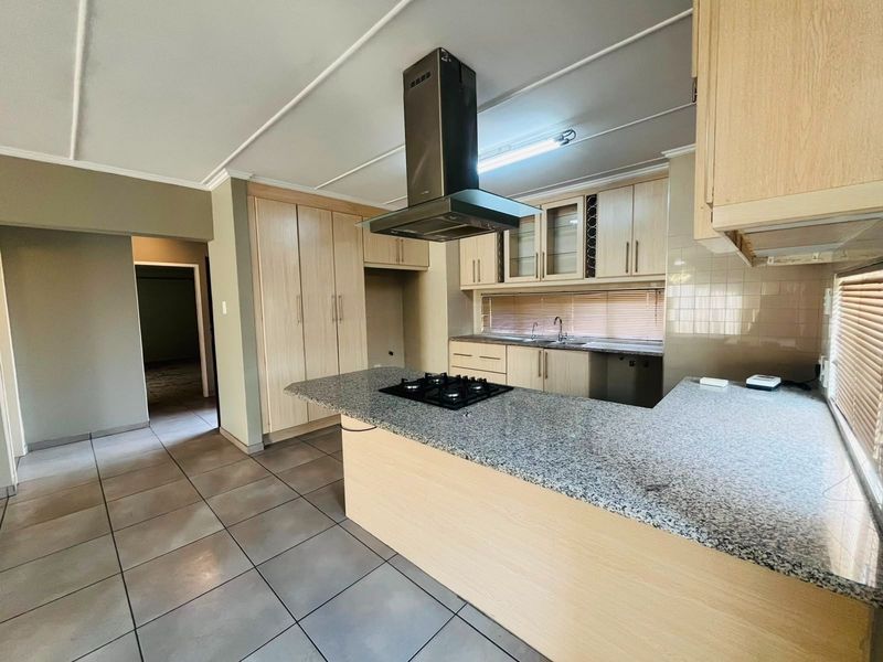 Spacious kitchen featuring light wood cabinetry, granite countertops, a central gas hob with extractor fan, and tiled flooring throughout.