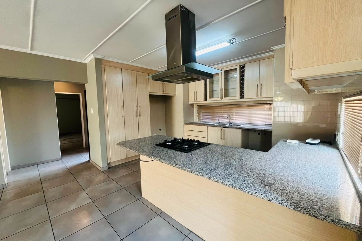 Spacious kitchen featuring light wood cabinetry, granite countertops, a central gas hob with extractor fan, and tiled flooring throughout.