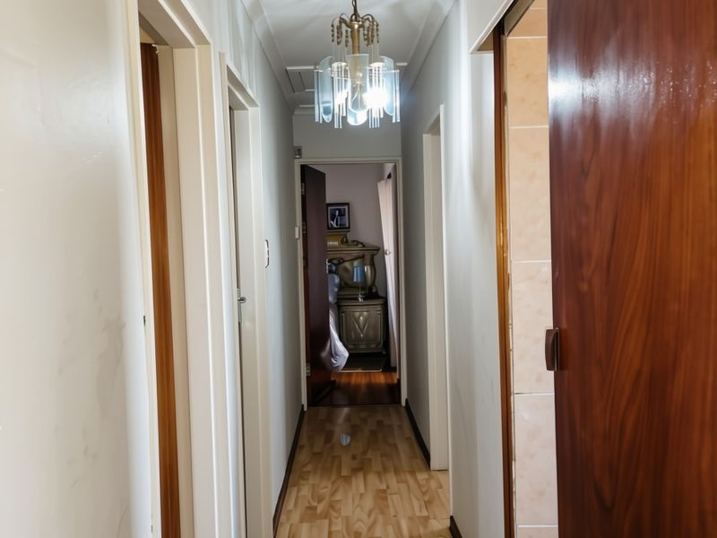A well-lit hallway featuring laminate flooring, classic cove cornicing, and a decorative chandelier, providing access to multiple rooms within the home.