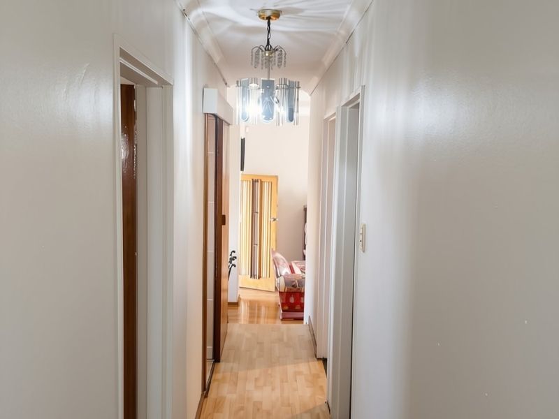 A functional hallway featuring light-toned laminate flooring, white walls, and classic cove cornicing, providing access to multiple rooms within the home.