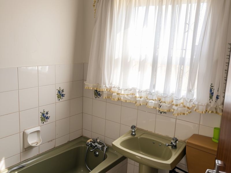 A dated bathroom featuring a green pedestal sink, matching bathtub, and toilet with classic floral-accented wall tiles.