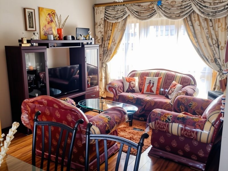 A living room featuring laminate flooring, a decorative crystal chandelier, and window treatments with a pelmet.