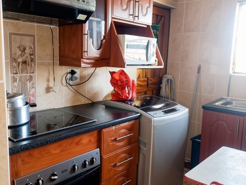 Compact kitchen featuring traditional wooden cabinetry, built-in oven and hob, extractor fan, and tiled finishes throughout.