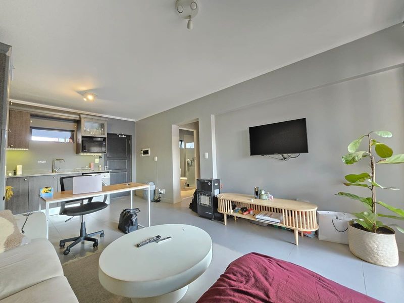 Open-plan living area featuring a modern kitchen with built-in cabinetry and appliances, seamlessly flowing into a comfortable lounge space with tiled flooring.
