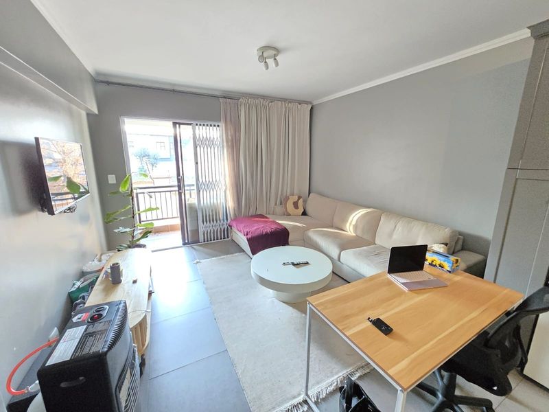 A well-lit living room featuring tiled flooring, neutral wall tones, and a sliding glass door providing access to a balcony with security gate.
