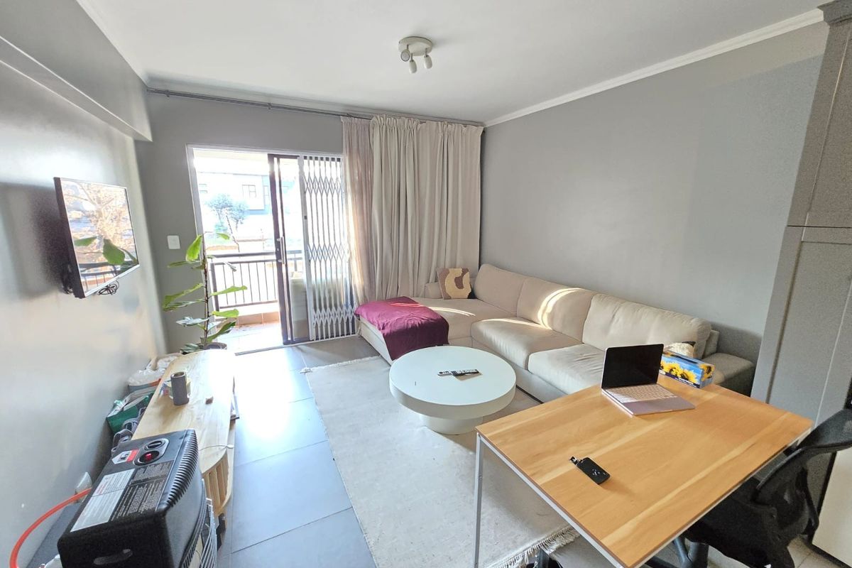 A well-lit living room featuring tiled flooring, neutral wall tones, and a sliding glass door providing access to a balcony with security gate.