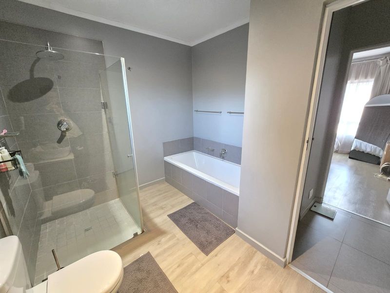 Modern bathroom featuring a glass-enclosed shower with a rain shower head, a built-in bathtub, and contemporary wood-look floor tiles.