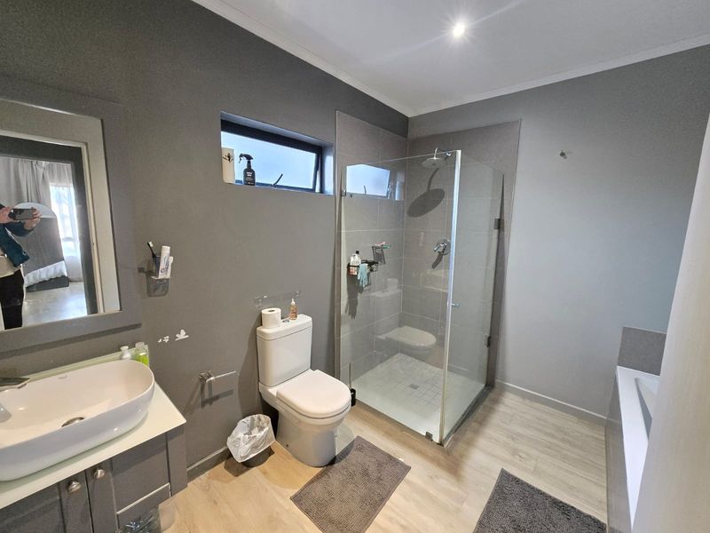 Modern bathroom featuring a vessel sink vanity, glass-enclosed shower with rain head, and a separate bathtub with neutral grey wall finishes.