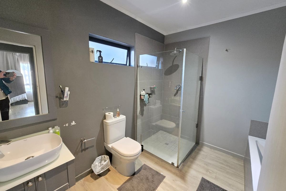 Modern bathroom featuring a vessel sink vanity, glass-enclosed shower with rain head, and a separate bathtub with neutral grey wall finishes.