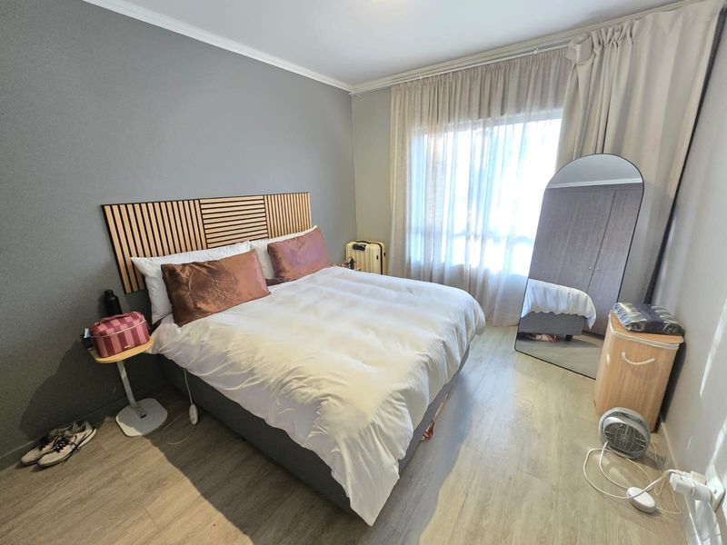 A well-maintained bedroom featuring light-toned laminate flooring, neutral grey walls, and a built-in wardrobe, offering a comfortable and functional living space.